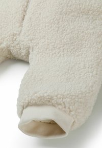 Crème-kleurige, textuurstof fleece kledingstuk met een zachte oppervlakte, elastische ribgebreide manchetten en een ritssluiting aan de voorkant.