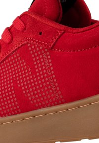 Crvene nubuk tenisice imaju perforirane detalje i otisnuti tekst "WORKS OF DENMARK." Gumeni potplat s smeškastim završetkom.