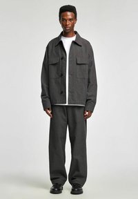 Szara, oversize marynarka w prążki z dwoma kieszeniami na piersi, czarne guziki, zestawiona z szerokimi spodniami. Całość dopełniają czarne skórzane buty.