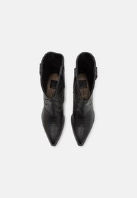 Botas de cuero negro hasta el tobillo con punteras afiladas y tiras laterales; presentan patrones de costura sutiles y una textura suave.