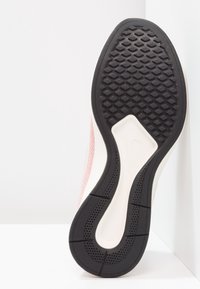 Nike-sneaker med en texturerad svart gummisula, krämfärgad mellansula och en rosa övre del med ett vävt mönster.