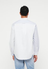 Πουκάμισο με κουμπιά σε ανοιχτό μπλε χρώμα με διακριτές λευκές ρίγες, που διαθέτει κλασικό γιακά και μακριά μανίκια. Μαλακό ύφασμα βαμβακιού, με ελαφρώς στρογγυλεμένο στρίφωμα.