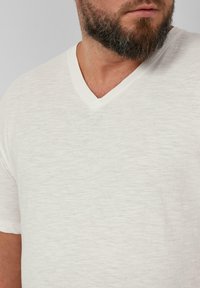 Witte v-hals t-shirt gemaakt van een zacht, textuurstof. Het ontwerp heeft korte mouwen en een relaxte fit, geschikt voor casual draag.