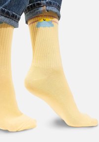 Żółte skarpetki prążkowane z jasnoniebieskim wzorem chmurki i słońca u góry. Posiadają gładką teksturę oraz standardową długość do kostki.