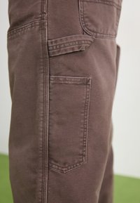 Braune Baumwoll-Cargohose mit einer Seitentasche und gestickten Details. Der Stoff weist eine strapazierfähige Textur auf und hat einen klassischen Schnitt.