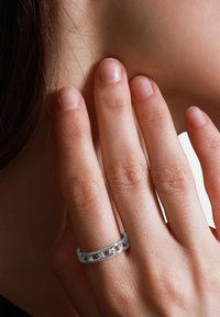 Zilveren ring met een kettinglinkdesign en een glad, gepolijst oppervlak. Draagt op een hand met natuurlijke, ongepolijste nagels.