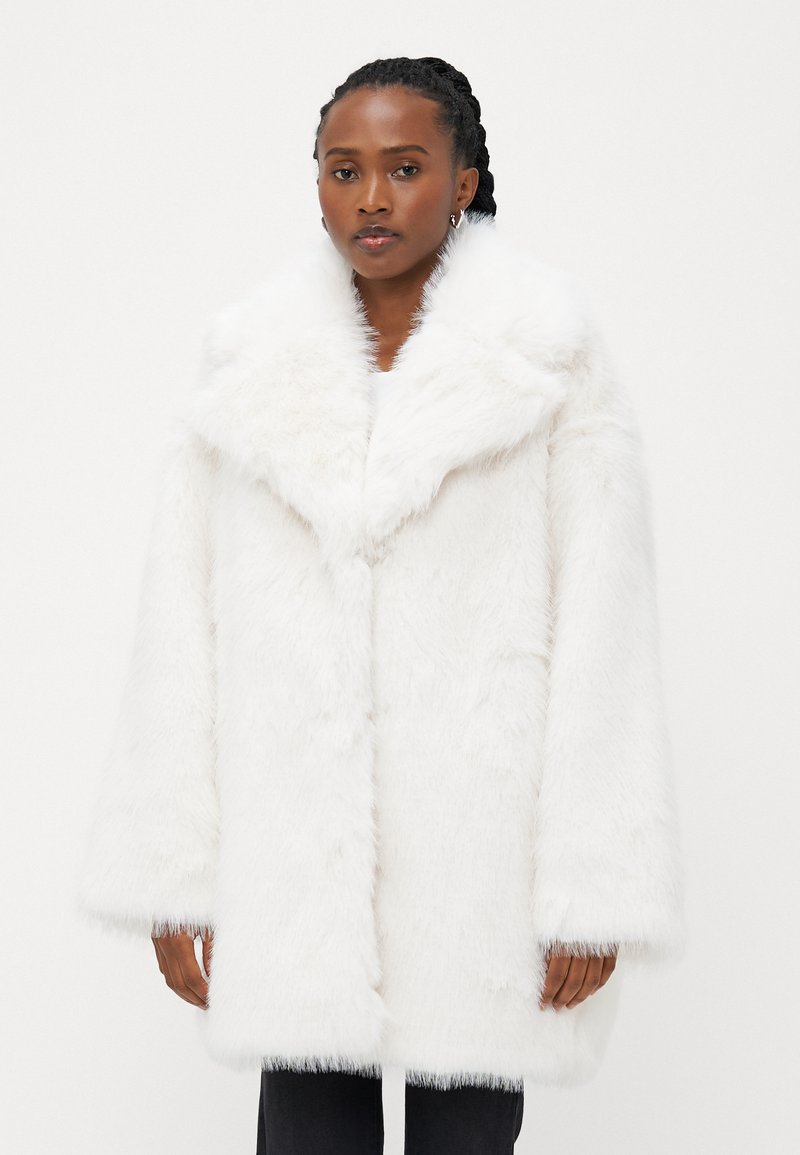 Biely kožuch s širokým golierom, dlhými rukávmi a jemnou textúrou. Má voľný strih a dĺžku po kolená.