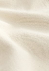 Tissu en coton d'un blanc cassé doux avec une surface lisse et texturée et un motif de tissage diagonal subtil. Léger et souple.