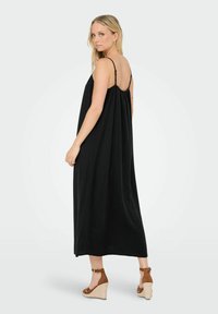 Svart ärmlös maxiklänning i mjukt tyg, med en rynkad design på baksidan. Matcher med bruna plattform wedgesandal.
