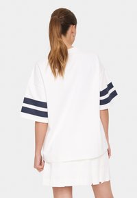 Camiseta blanca de gran tamaño con rayas azul marino en las mangas cortas, con un escote redondo y un corte relajado, combinada con una falda blanca con plisados.