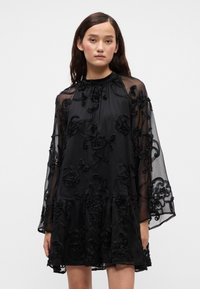 Crna haljina od prozirnog materijala, sa cvjetnim vezom, dugim rukavima, nabranim izrezom i višeslojnim rubom.