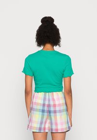 Krótki rękaw, zielona krótka koszulka z falbankowymi krawędziami, zestawiona z wielokolorowymi szortami w kratkę z elastycznym pasem.