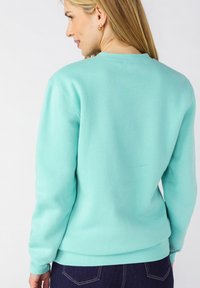 Felpa blu turchese chiaro con collo tondo, maniche lunghe, polsini a costine e una texture liscia; minimalismo evidente sul retro.