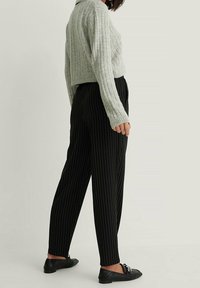 Jasnoszary, żeberkowany, krótki sweter, czarne spodnie w prążki z wysokim stanem oraz czarne mokasyny z metalicznymi akcentami. Gładkie i strukturalne tekstury.