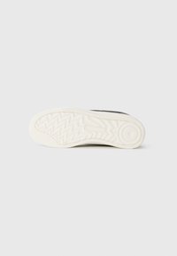 Black sneaker sole with a textured white rubber outsole, featuring a zigzag pattern and a circular accent near the heel.