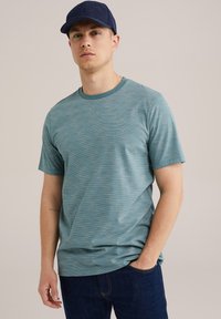 Lys teal kortærmet t-shirt med stribet tekstur. Rund halsudskæring og afslappet pasform. Bæres med mørk denim jeans og en marineblå kasket.