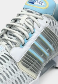 Κοντινό πλάνο ενός λευκού και γαλάζιου αθλητικού παπουτσιού με υφασμάτινο δίχτυ, πλαστικά επικαλύμματα και λευκούς κορδόνια περασμένα μέσα από τρύπες.