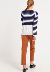 Striped navy and white long-sleeve top with a white bottom layer, paired with brown tapered pants and black shoes. Smooth texture, casual design.