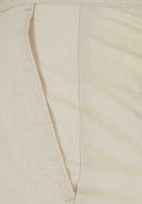 Gros plan sur un tissu beige avec des coutures visibles et des détails de couture sur un vêtement, montrant la texture et le tissage du matériau.