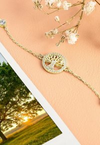 Bracciale color oro con un ciondolo a forma di albero della vita circolare adornato da pietre trasparenti e scintillanti. La catena è delicata con anelli rotondi.