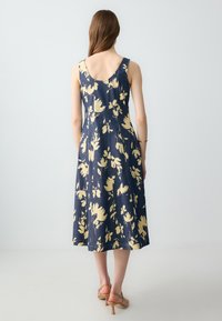 Ärmelloses Kleid mit Blumenmuster in Marineblau und Gelb, mit figurbetontem Oberteil und schwingendem Rock, aus leichtem Stoff gefertigt.
