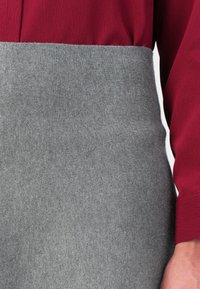 Chemise rouge à manches longues rentrée dans une jupe en maille grise taille haute, montrant la taille et le bras droit de la personne.