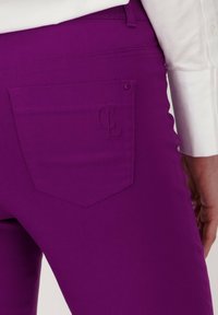 Paarse broek met een zak en een subtiele reliëflogo. De stof is glad, met een slim fit ontwerp en nette stiksels op de naden.