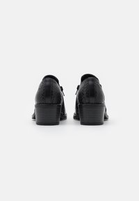 Scarpe nere con una finitura a trama rettile, design curvo e tacco basso a blocco. Presentano una punta arrotondata e liscia con dettagli di cucitura sottili.