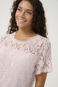Top in pizzo rosa chiaro con maniche corte, scollatura ondulata e motivi floreali intricati su tutta la superficie. Tessuto morbido e design femminile.