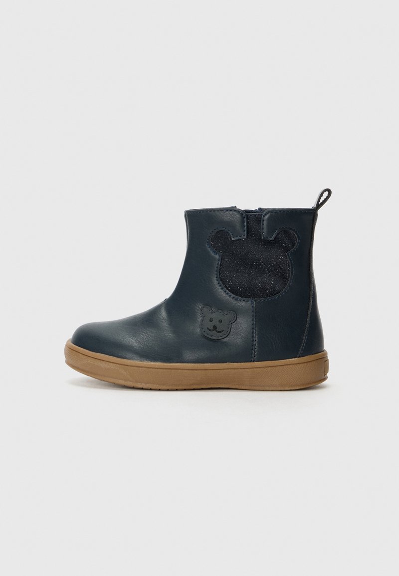 Botas de tobillo de cuero azul marino con acentos en forma de oso, suela de goma y un parche texturizado de un tono azul oscuro en la parte trasera; cierre con cremallera.