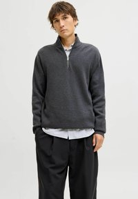 Hallhalline lukuga sviiter, millel on tekstureeritud kangas ja kõrge krae. Kantud sinise ja valge triibulise särgi üle, koos laia musta pükstega.