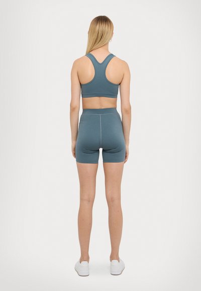 Zeleno-modrý športový crop top a šortky, priliehavý strih, hladká látka, s pretekárskym zvrškom a šortkami so stredným pásom, doplnené bielymi teniskami.