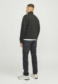 Sudadera negra con cuello alto, combinada con jeans oscuros y zapatillas deportivas claras. La sudadera presenta una textura suave y un diseño minimalista.