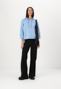 Felpa blu chiaro con cappuccio, dal design corto e con cordini, abbinata a pantaloni neri a gamba larga e scarpe piattaforma nere.