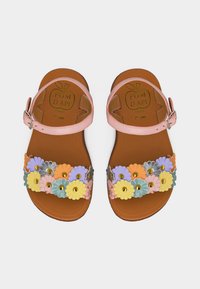 Καφέ δερμάτινα σανδάλια με ροζ λουριά στον αστράγαλο και πολύχρωμες διακοσμητικές ανθοστοιχίες πάνω από τα δάχτυλα, στερεωμένες με χρυσά καρφιά.