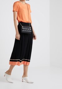 Svart plisserad midikjol med orange och vit fåll, kombinerad med en lysande orange t-shirt, en svart handväska med pärldetaljer och vita mules.