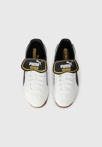 Hvite fotballsko med svarte detaljer, teksturert overdel, snøring og stor svart rem merket "PUMA KING" i gult på tungen.