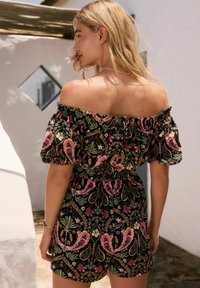 Svart off-shoulder jumpsuit med ett blommönster i rosa och grönt, puffärmar och ett elastiskt midjeband för en figurnära passform.