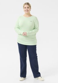 Lange mouw, lichtgewicht, groen en wit gestreept T-shirt met een ronde hals, gecombineerd met donkerblauwe jeans en witte sneakers.