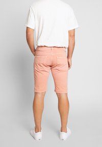 Shorts de mezclilla rosa claro con bolsillos delanteros y traseros, dobladillos enrollados y un diseño ajustado. Combinados con una camiseta blanca básica.