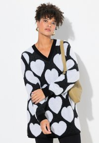 Zwart-witte trui met een V-hals, lange mouwen, zachte textuur en hartpatronen. Zwarte manchetten en zoom. Gestyled met een beige tas.