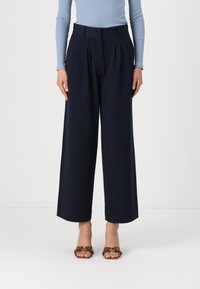 Navy wide-leg trousers with pleats, tailored waistband, and soft fabric. Paired with brown strappy sandals. The top is light blue ribbed.