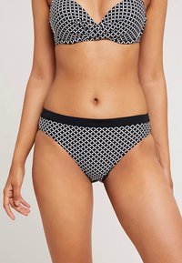 Conjunto de bikini com padrão geométrico a preto e branco, com um top estilo bandeau torcido e calções de corte baixo com uma cintura preta contrastante.