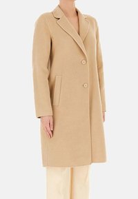 Cappotto di lana beige con rever appuntito, due bottoni, tasche laterali e vestibilità su misura. Tessuto liscio e design lungo fino al ginocchio.