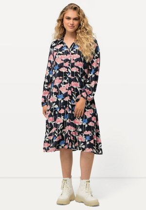 Abito floreale con maniche lunghe, pieghe, sfondo nero e motivi rosa e blu; abbinato a stivali platform bianchi.