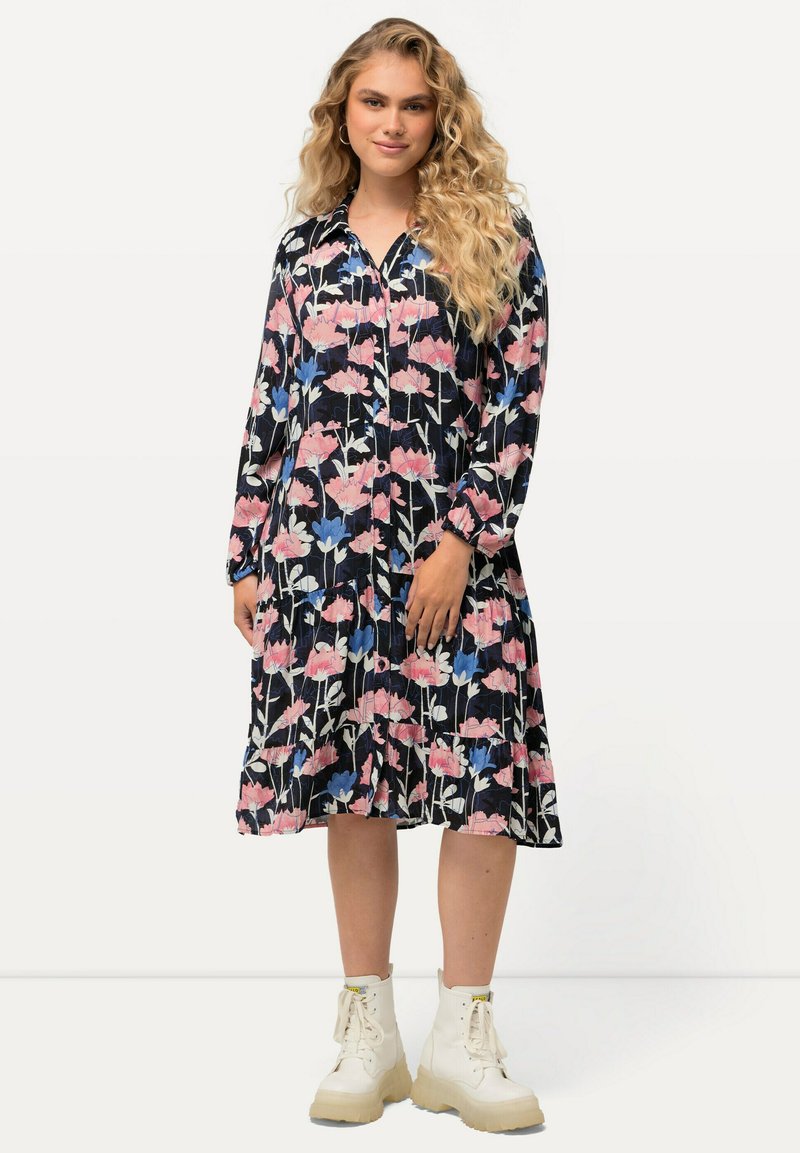 Kukallinen mekko pitkilla hihoilla, poimuja, musta tausta sekä vaaleanpunaisia ja sinisiä kuvioita; yhdistetty valkoisiin platform-korkeisiin saappaisiin.