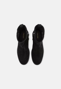 Stivaletti alla caviglia in suede nero con una texture liscia, zip laterale e design a punta arrotondata. L'interno presenta un marchio dorato.