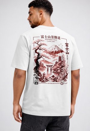 Man wearing white t-shirt with red Japanese landscape design featuring Mount Fuji, cherry blossoms, pagoda, torii gate, and Japanese text.
