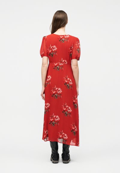 Naine kannab punast lillelist keskmise pikkusega kleiti lühikeste õhuliste varrukatega, seisab seljaga kaamera poole, koos mustade saapadega.