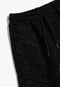 Sorte joggerbukser lavet af struktureret stof, med elastisk talje og snoretræk samt sidelommer. Let grå spræl i hele stoffet.